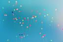 Dozens of small, brightly coloured balloons drifting upward against a clear blue sky.