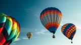 Assorted color hot air balloons floating in a clear sky.